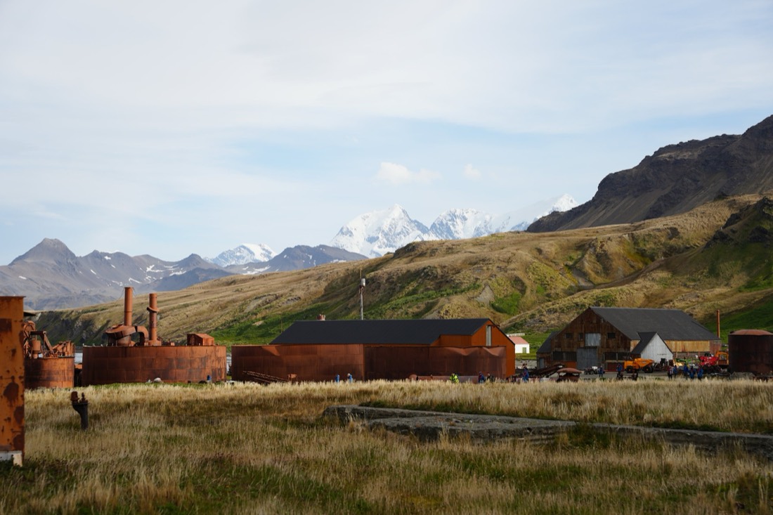 Rusted tanks and buildings of an abandoned whaling station beneath snowy peaks, South Georgia