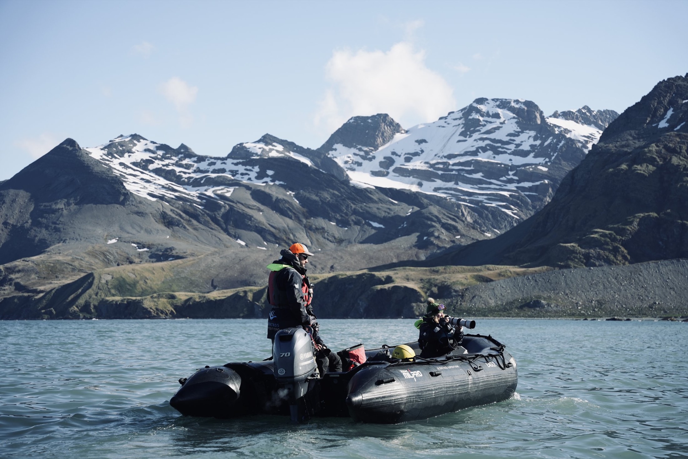 Expedition Zodiac with a photographer and guide beneath snow-streaked mountains, South Georgia