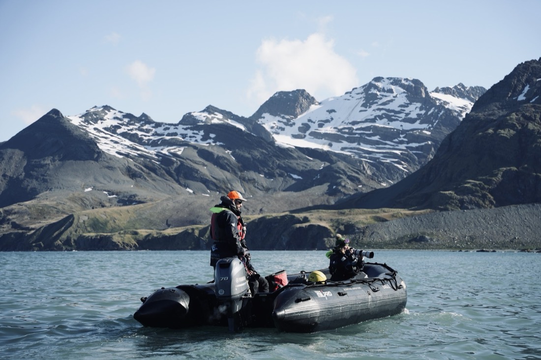 Expedition Zodiac with a photographer and guide beneath snow-streaked mountains, South Georgia