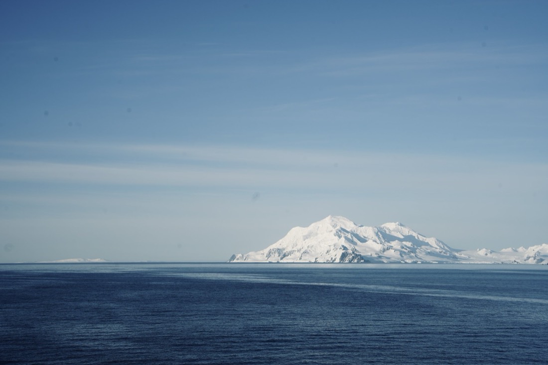 Snow-covered island on the horizon across a calm deep-blue Antarctic sea