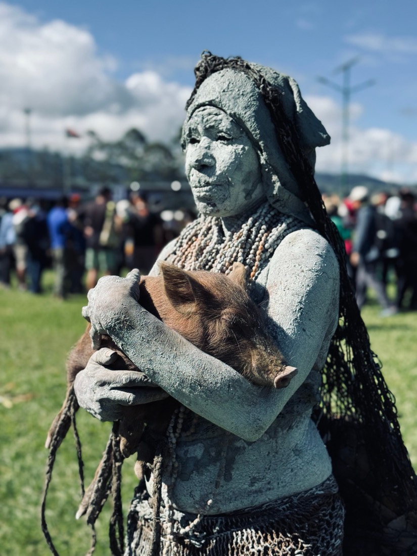 A woman covered head to toe in grey clay holds a piglet to her chest at a Highlands show in Papua New Guinea