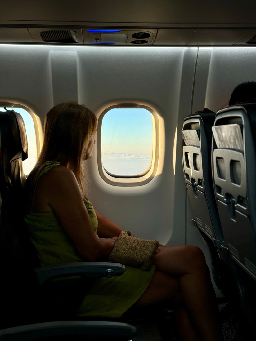A passenger in a quiet aircraft cabin looks out of an oval window at a pale sky
