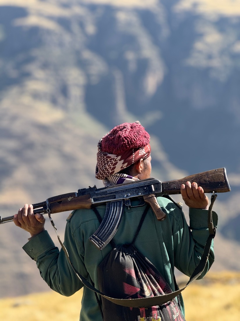 A park scout in a red knitted cap carries a rifle across his shoulders above the cliffs of the Simien Mountains, Ethiopia