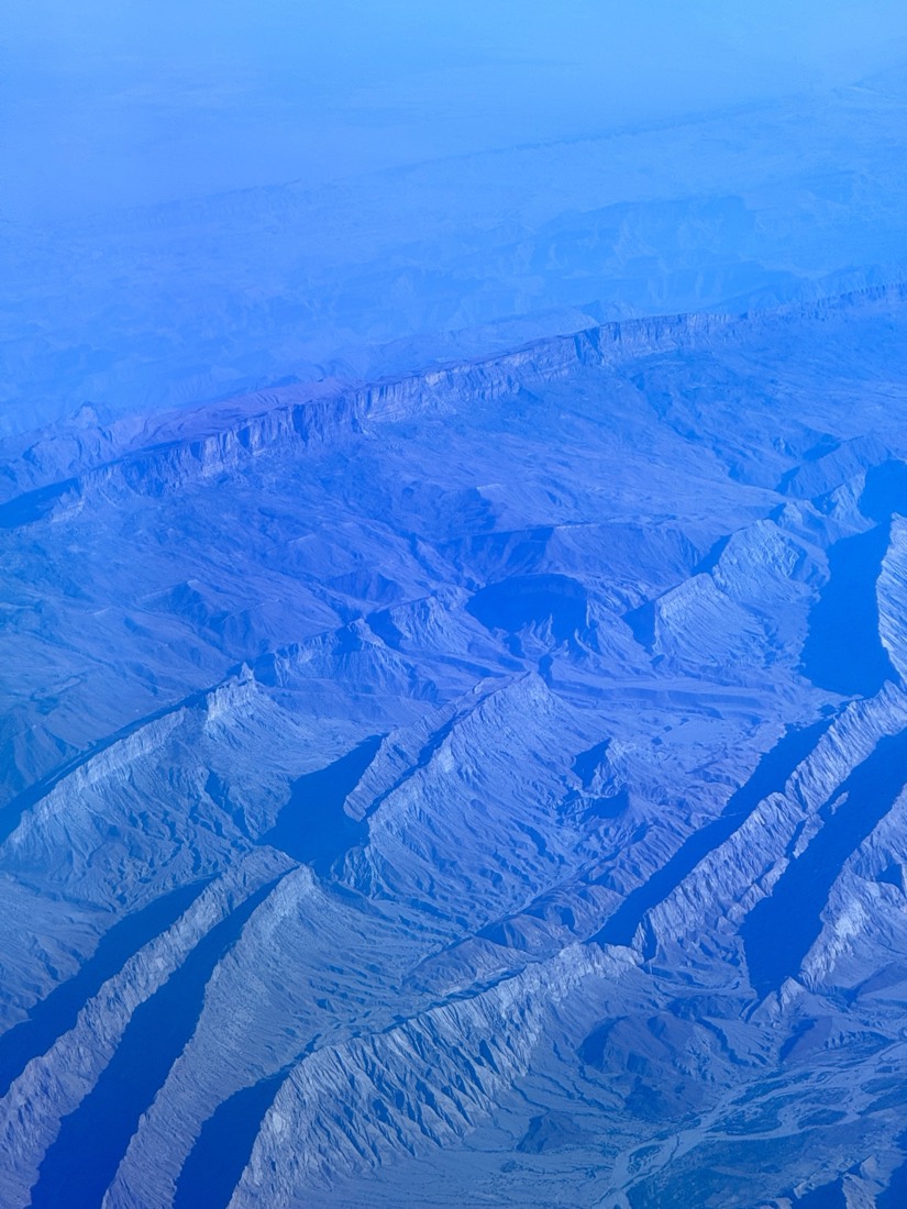 Folded ridges and dry valleys turned blue in haze, seen from a plane window