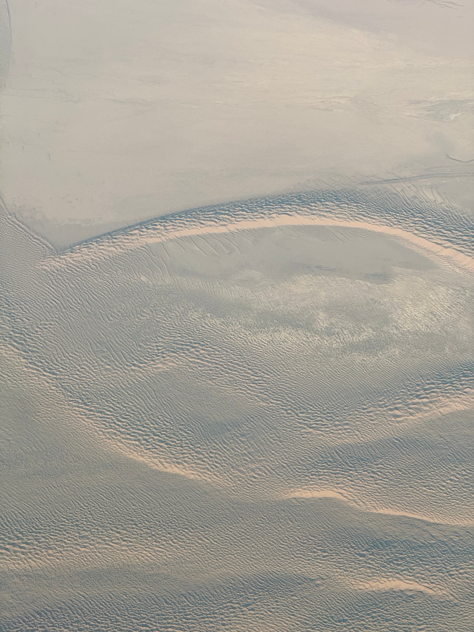 Wind-drawn ripples and curves across a pale desert seen from high above