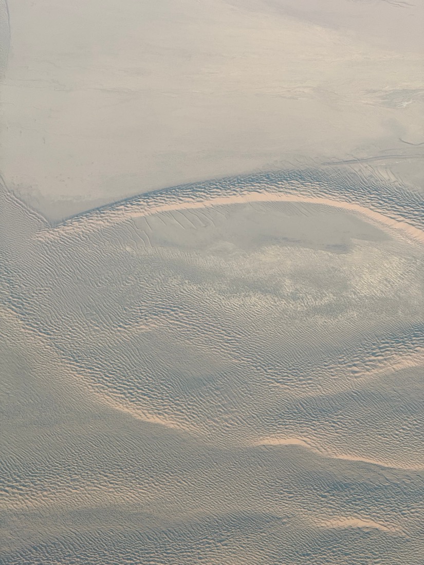 Wind-drawn ripples and curves across a pale desert seen from high above