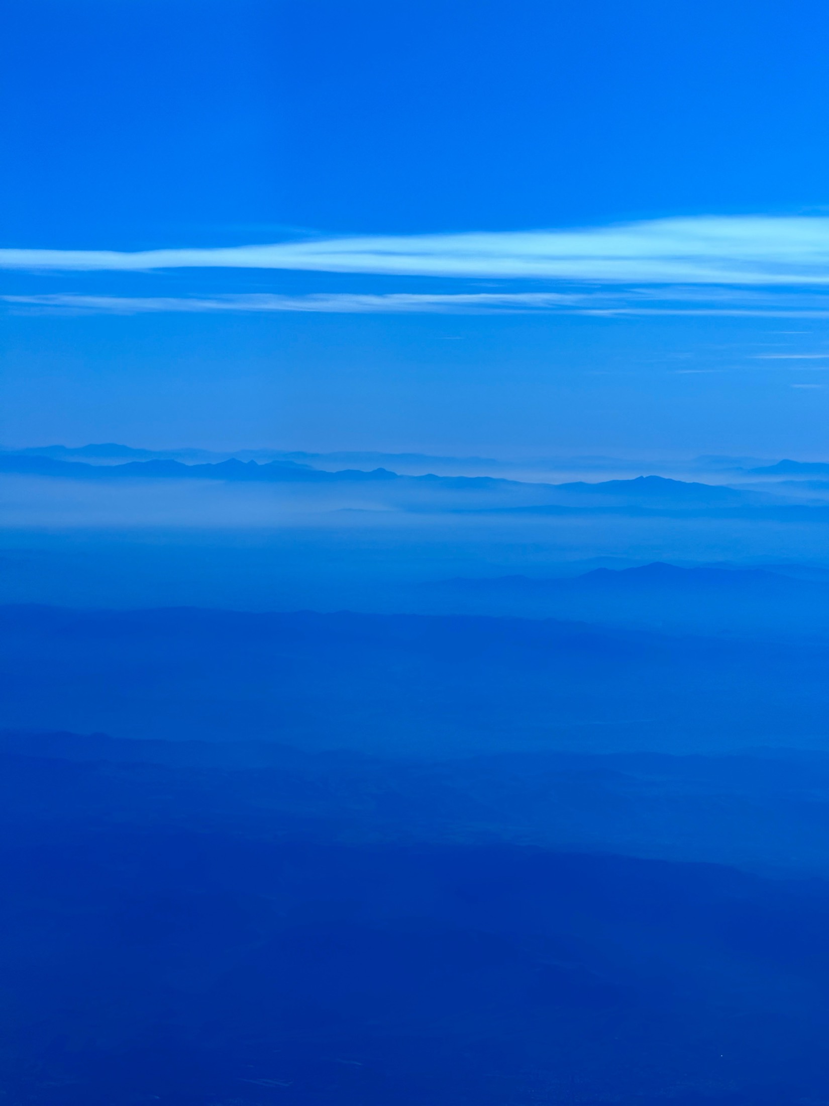A thin band of cloud on the horizon over a deep blue sea, from a plane window