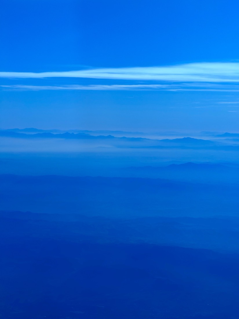 A thin band of cloud on the horizon over a deep blue sea, from a plane window