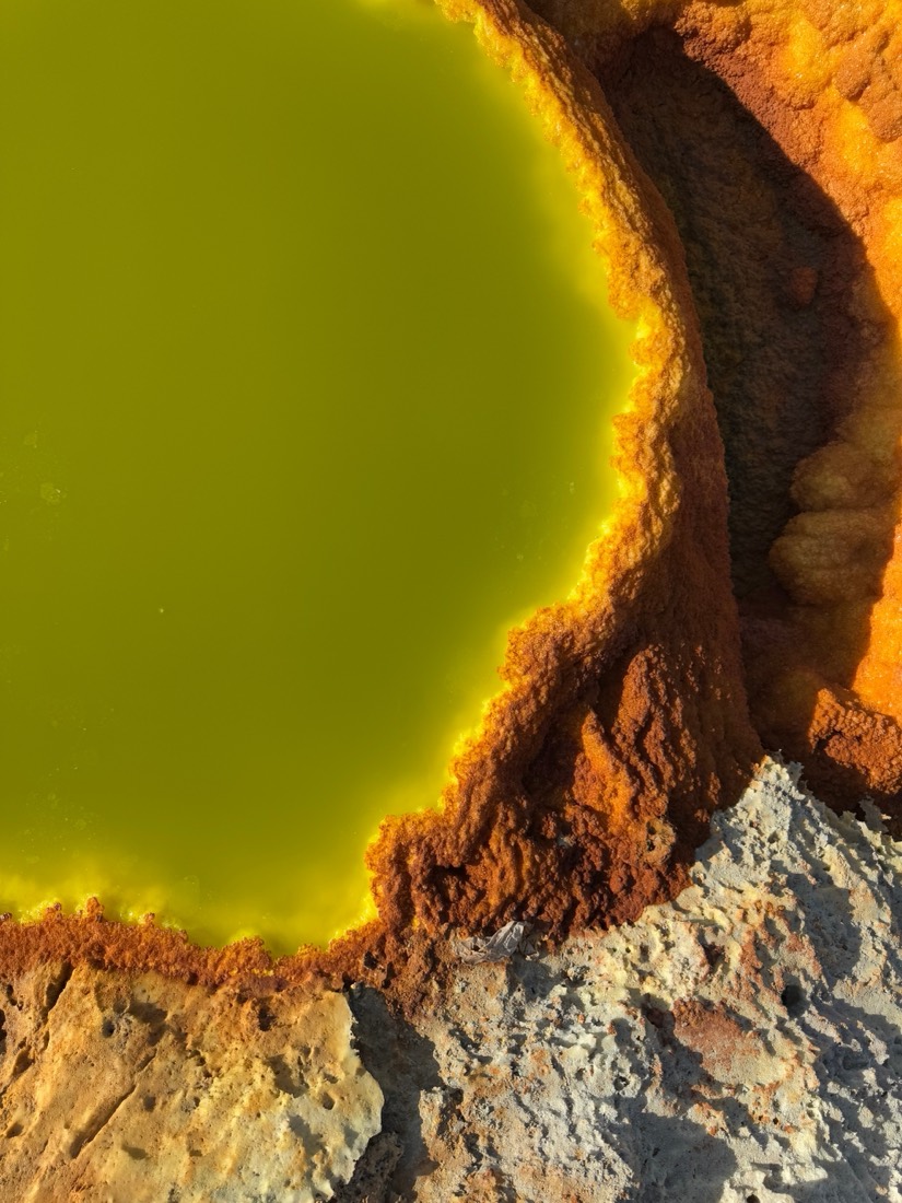 A pool of acid-yellow water ringed by orange and white mineral crust in the Danakil Depression, Ethiopia