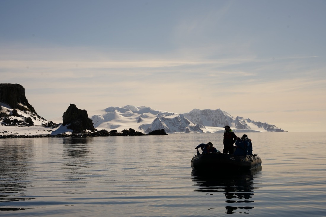 Zodiac drifting at dusk on glassy water below glaciated Antarctic mountains