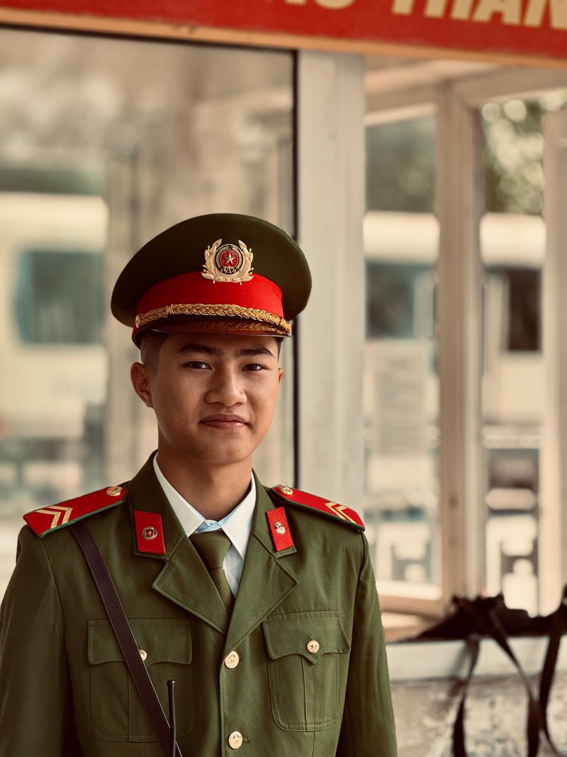 A young Vietnamese soldier in an olive uniform and red-banded cap stands in a doorway in Hanoi