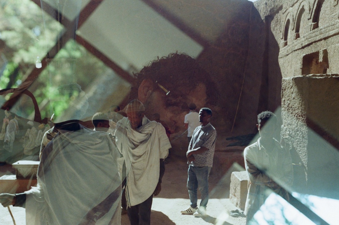 Men in white shawls glimpsed through a window and its reflection, shot on film