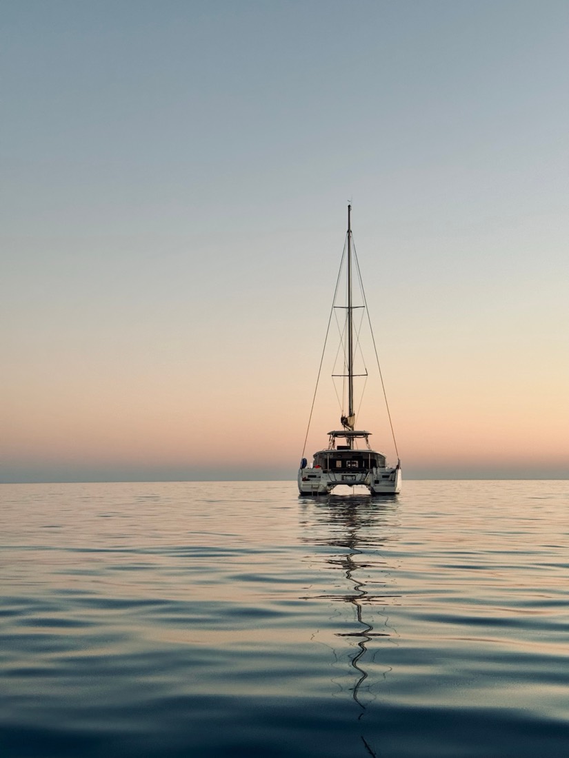 A catamaran and its reflection on glassy water under a peach and blue dusk, Sardinia