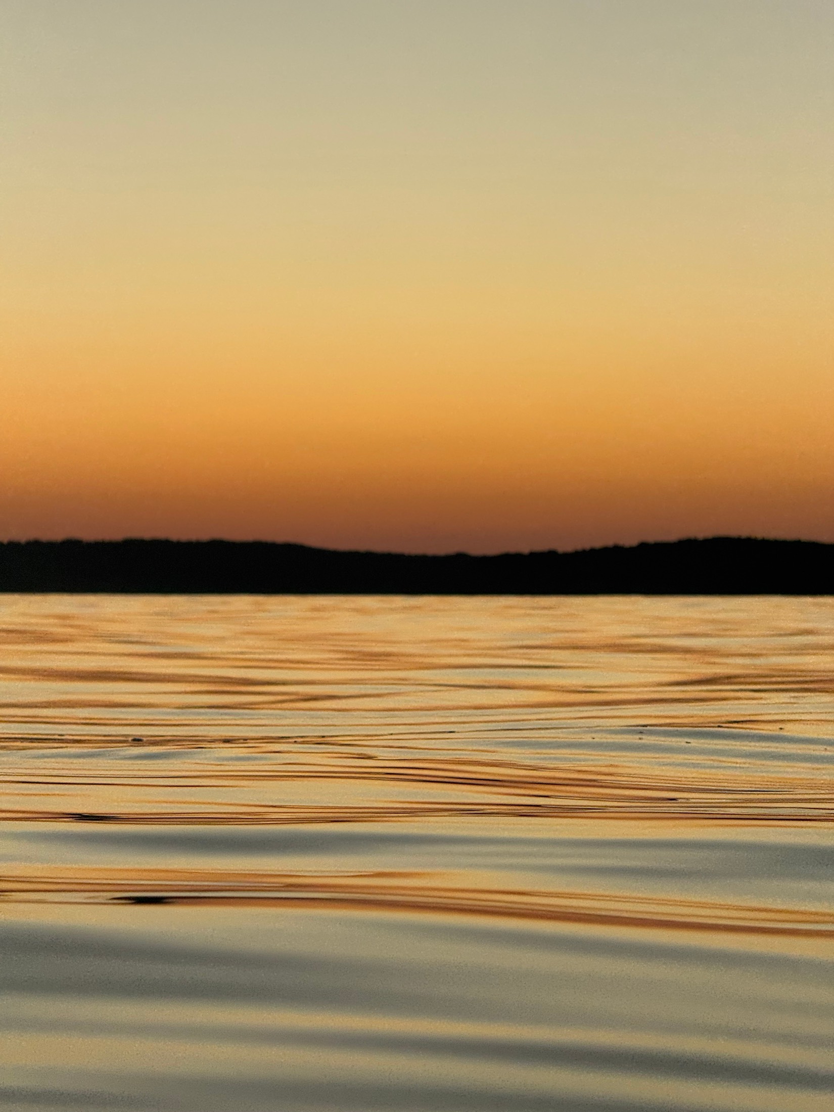 Gold and blue ripples on the sea beneath a dark headland at sunset, Sardinia