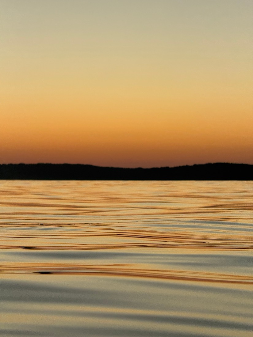 Gold and blue ripples on the sea beneath a dark headland at sunset, Sardinia
