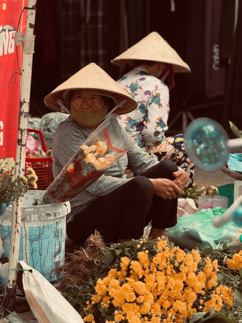 Two women in conical hats sell bunches of yellow flowers at a market in central Vietnam