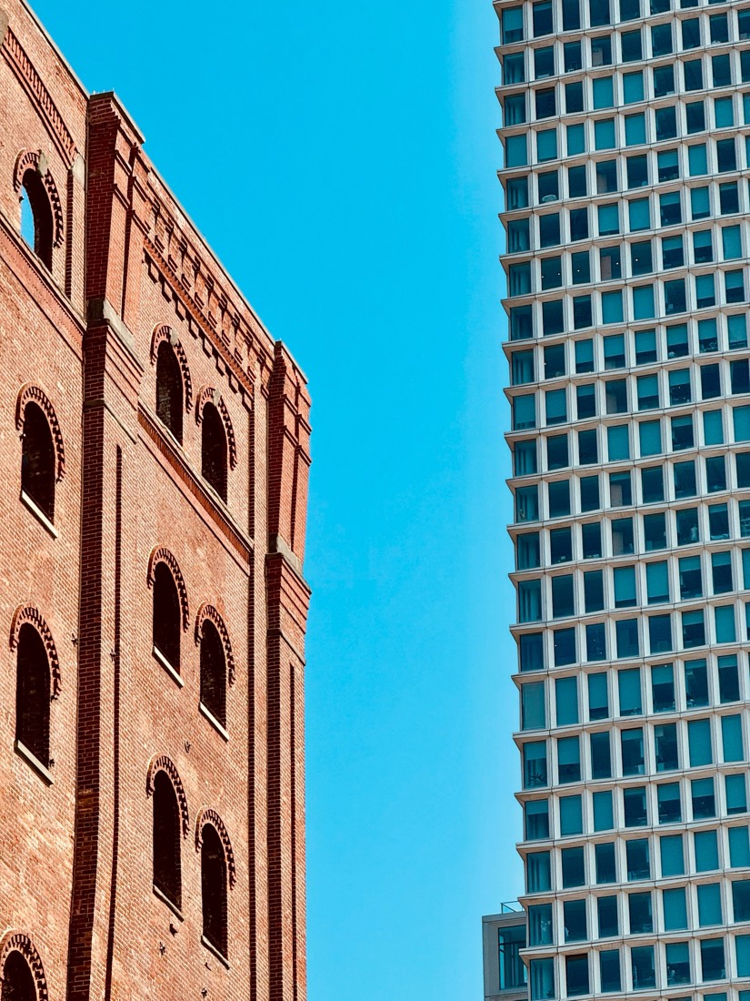 An old red-brick warehouse with arched windows beside a glass tower, against a blue sky in Brooklyn