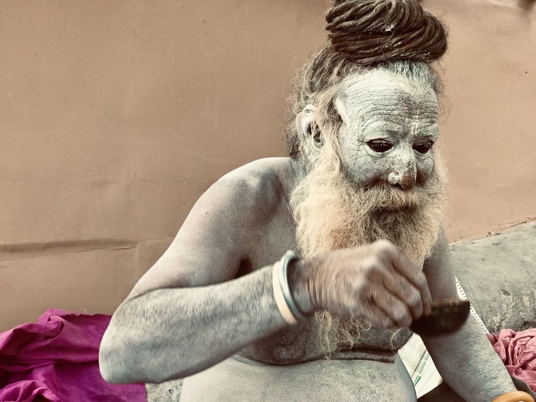Ash-covered holy man with a long beard and coiled dreadlocks, eating