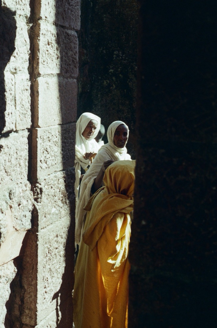 Women in white and saffron robes stand in the stone doorway of a rock-hewn church, on Fujifilm 400 film, Ethiopia