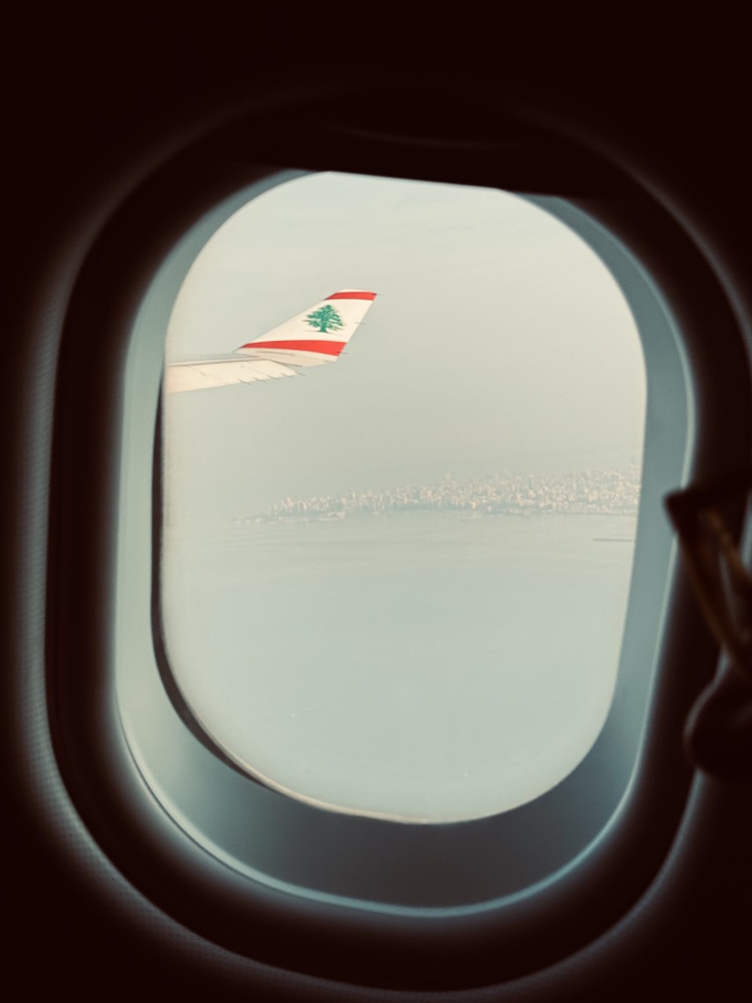 Aeroplane window looking out at a red-and-white wingtip over a hazy coastline