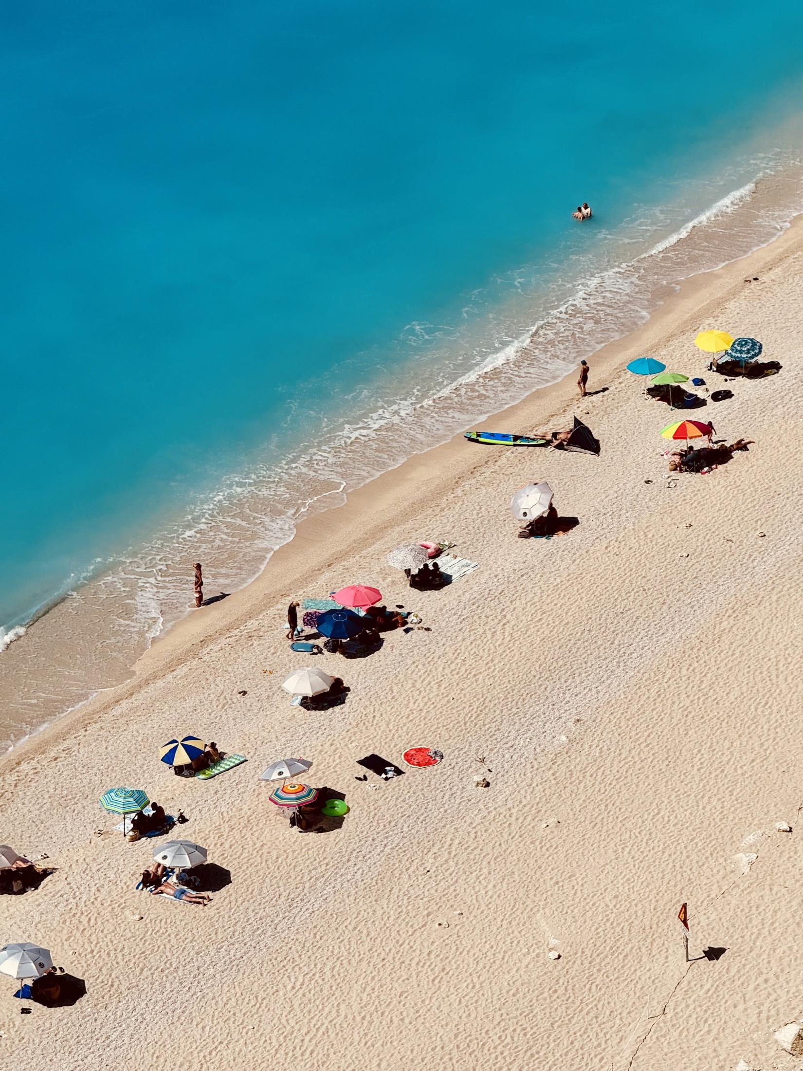 Aerial view of colourful beach umbrellas on white sand beside a turquoise sea