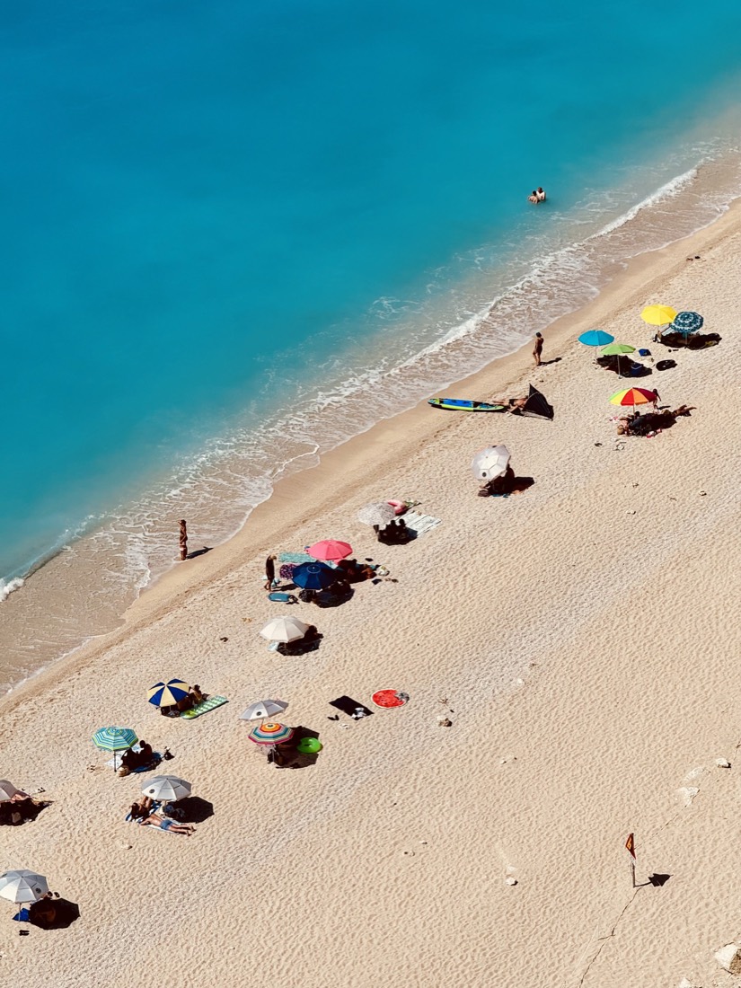 Aerial view of colourful beach umbrellas on white sand beside a turquoise sea