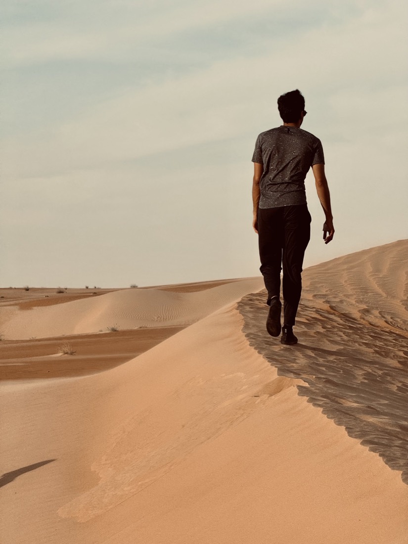 Man walking alone along the ridge of a red sand dune