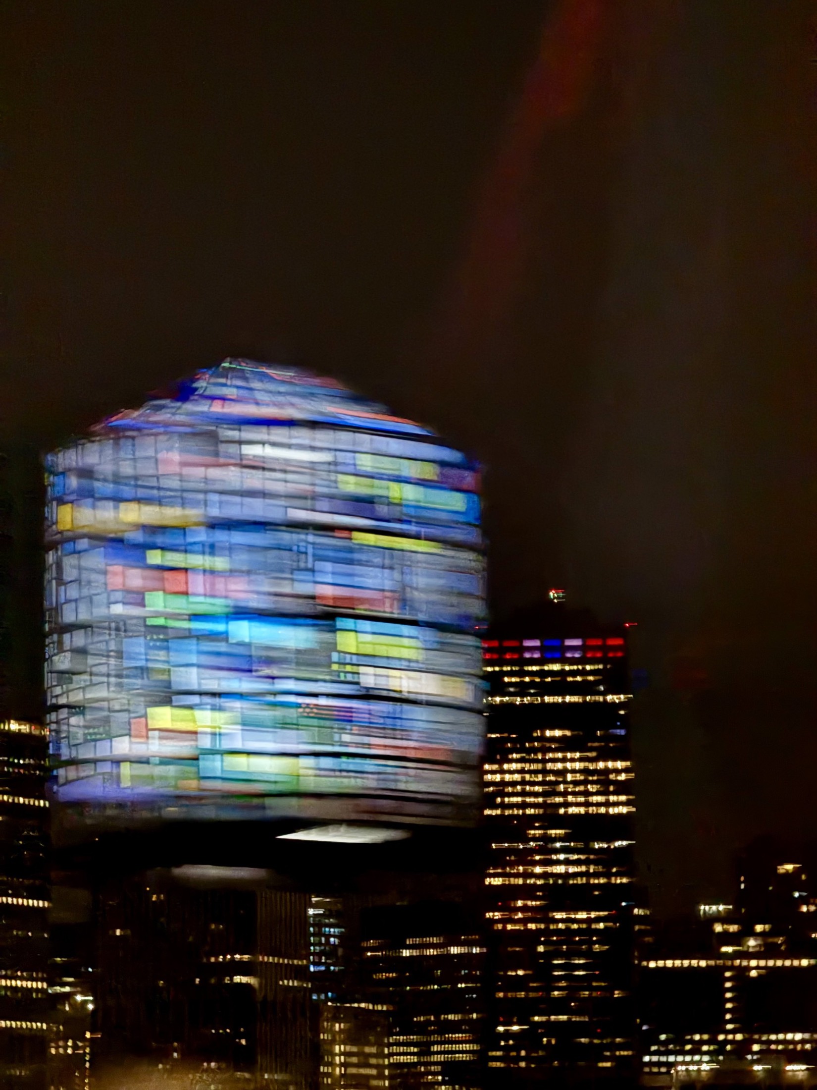 Illuminated tower glowing with coloured light above a city at night