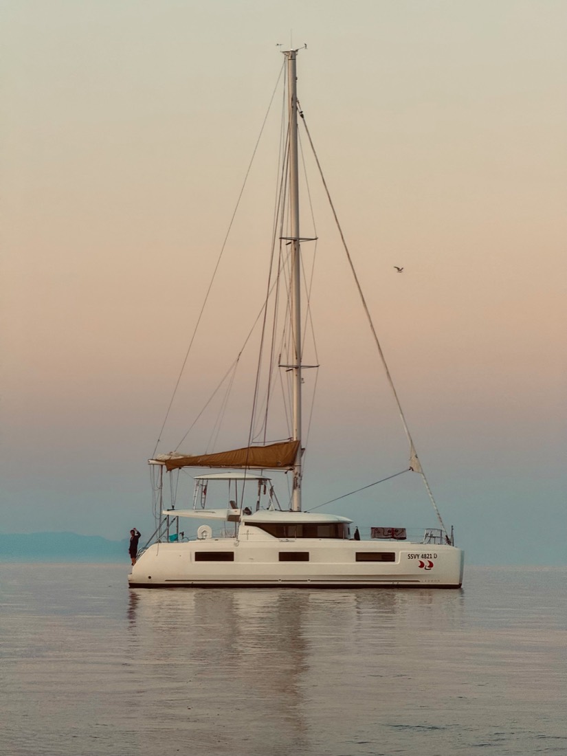 Catamaran at anchor on still water under a pastel dusk sky