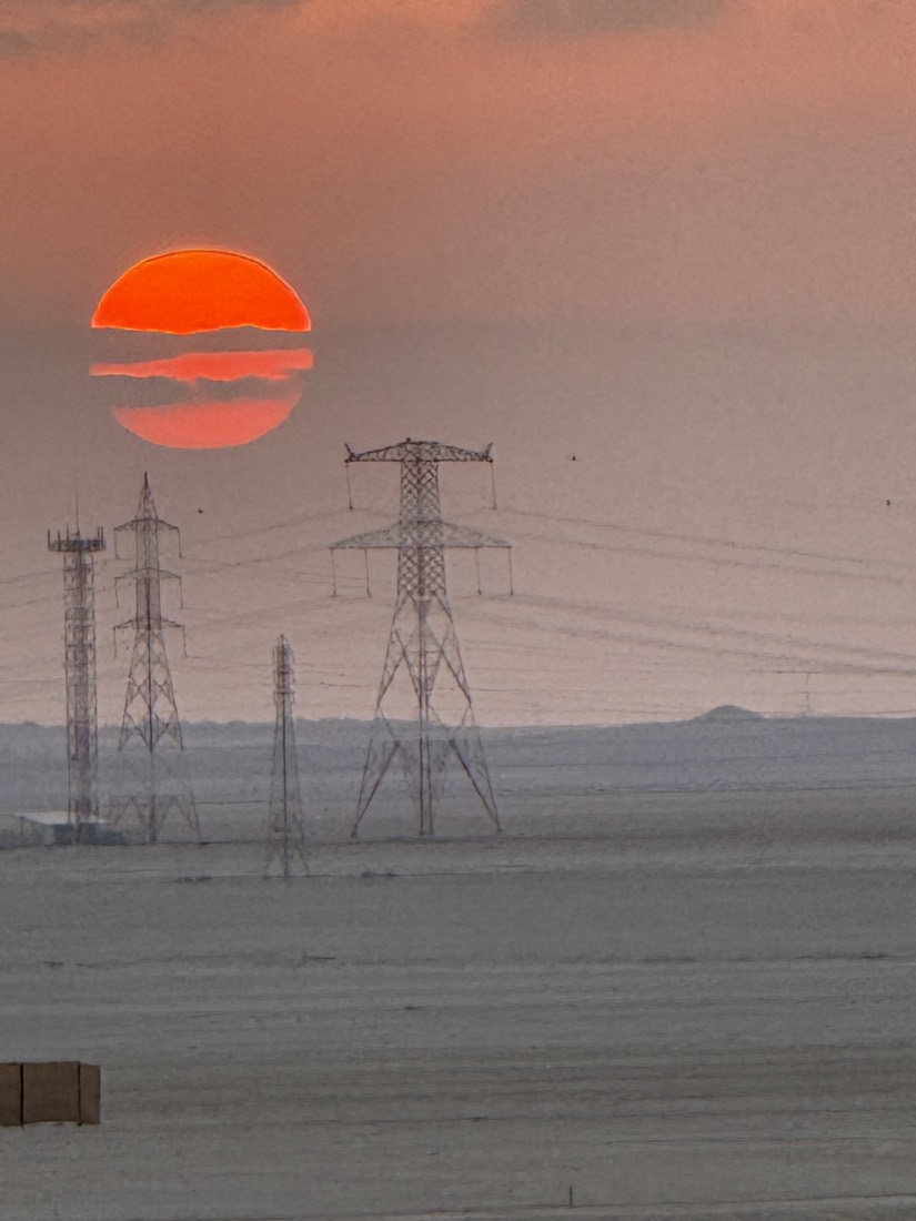 Red sun setting through haze behind power pylons