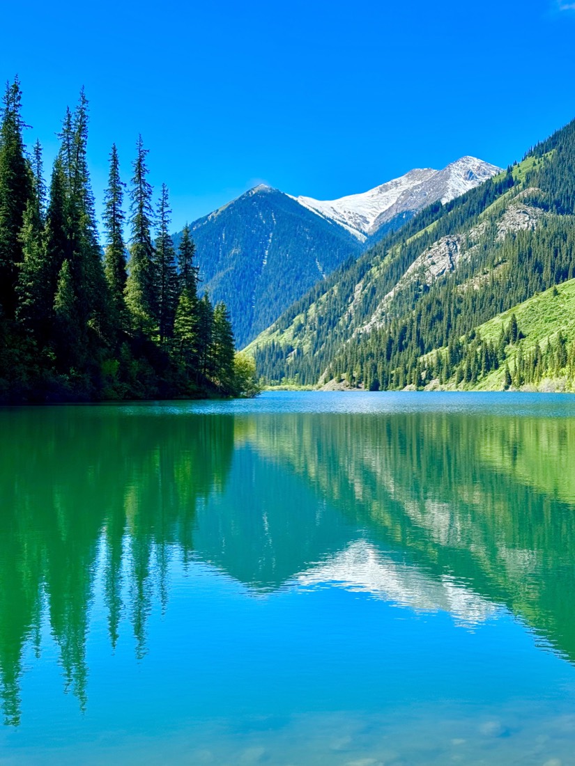 Mirror-still turquoise lake reflecting pine forest and mountains