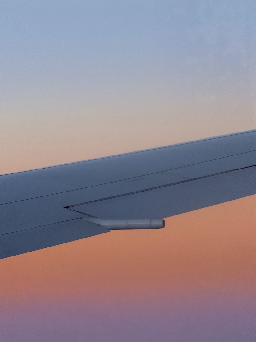 Aircraft wing over a pink and orange sunset sky