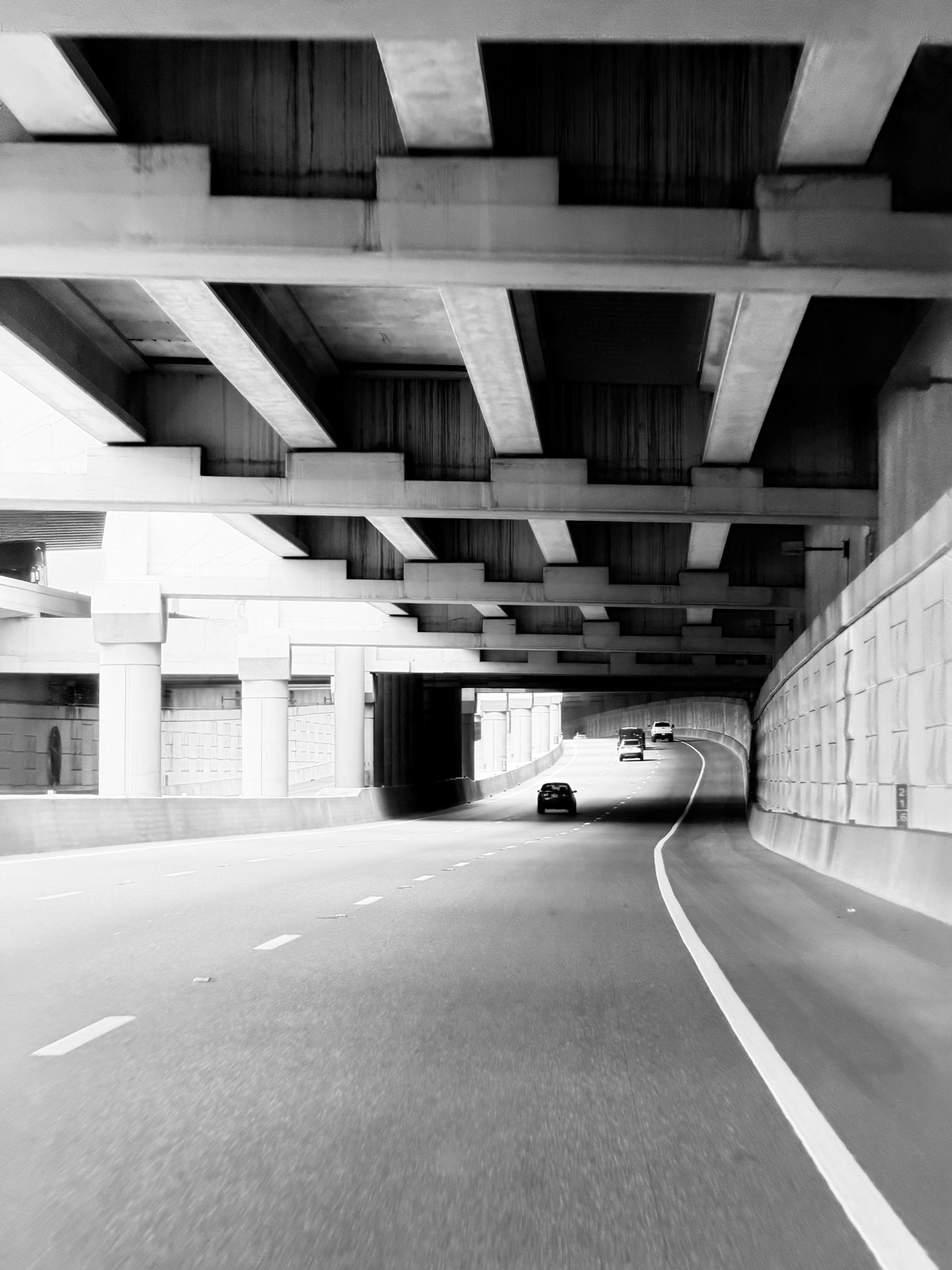 Empty road beneath a concrete overpass, black and white