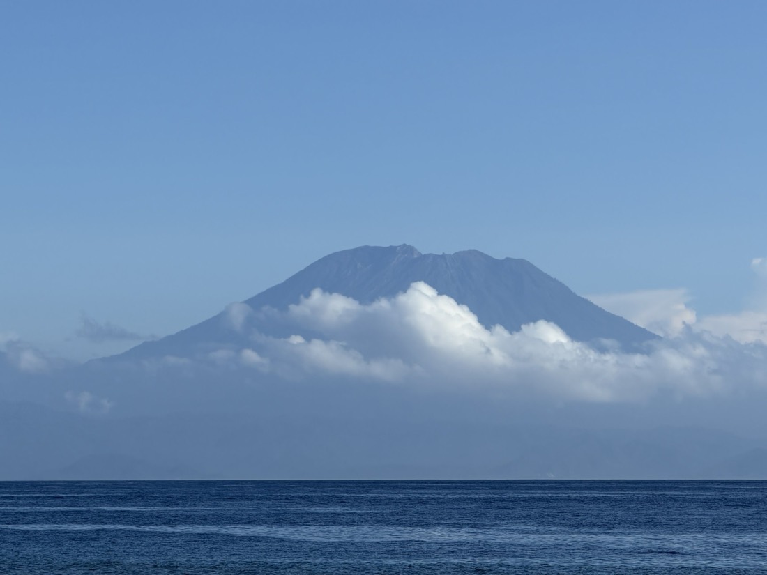 Volcano rising above a band of white clouds over a deep blue sea