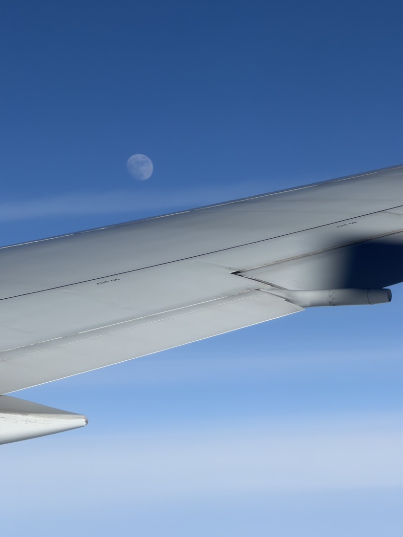 Aircraft wing and a daytime moon in a blue sky
