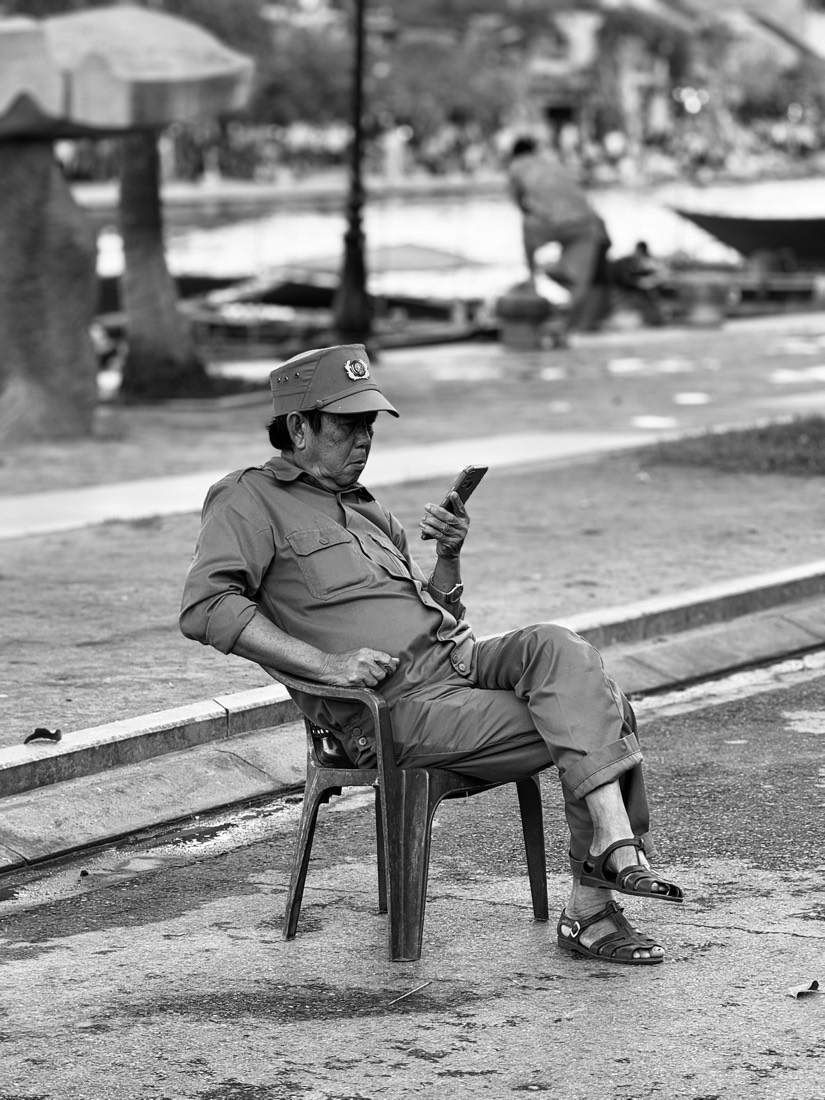 Elderly man resting in a chair beside a path, black and white