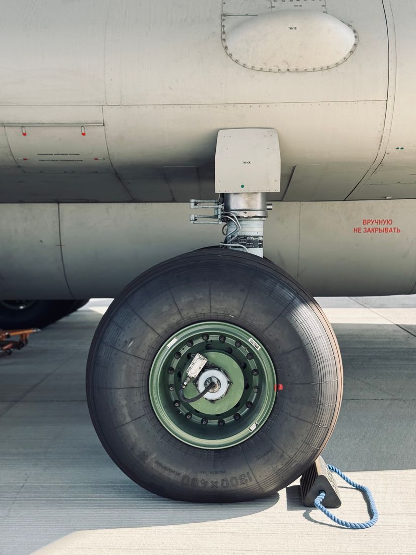 Main wheel of a Soviet-era aircraft, green hub and chock on the apron, Cyrillic stencilling on the fuselage