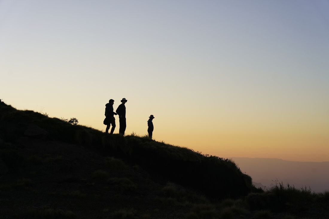 Three figures silhouetted on a grassy ridge against a gold and blue dusk sky