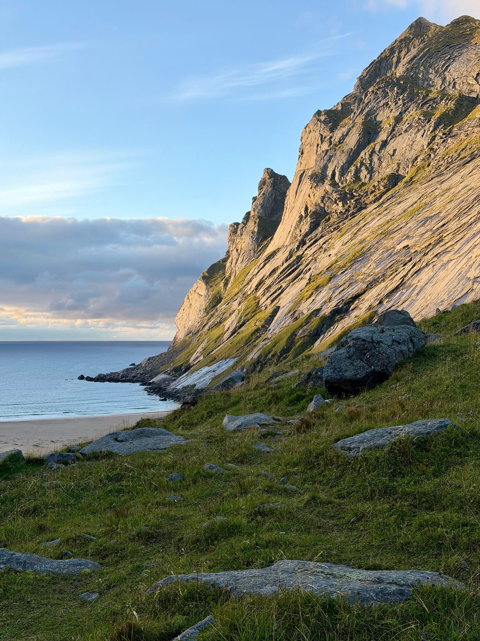 Steep sunlit granite ridge dropping to a white-sand beach and calm sea, Lofoten, Norway