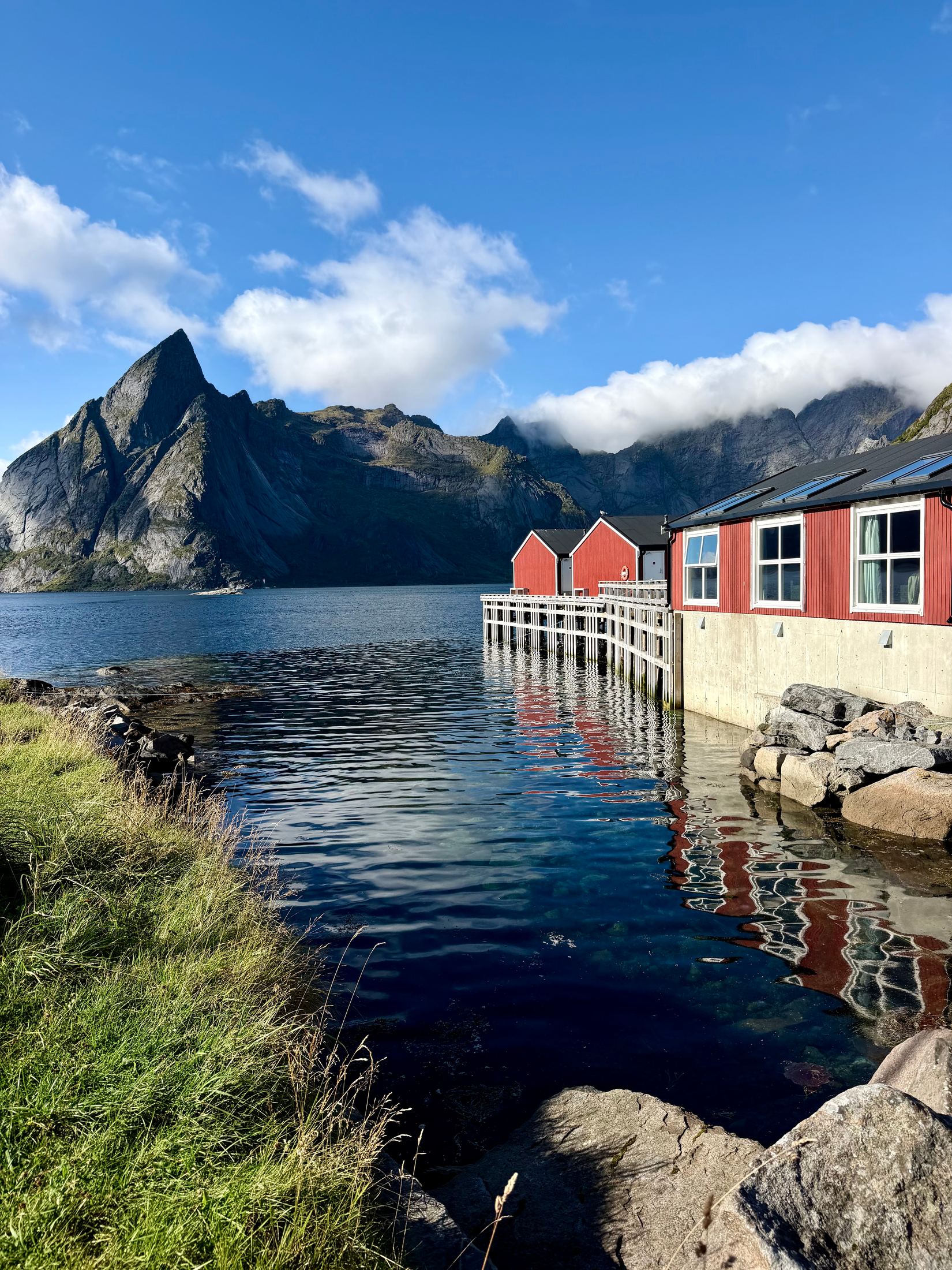Red rorbu, the traditional fishermen's cabins on stilts, beside a still fjord below a sharp peak, Lofoten, Norway