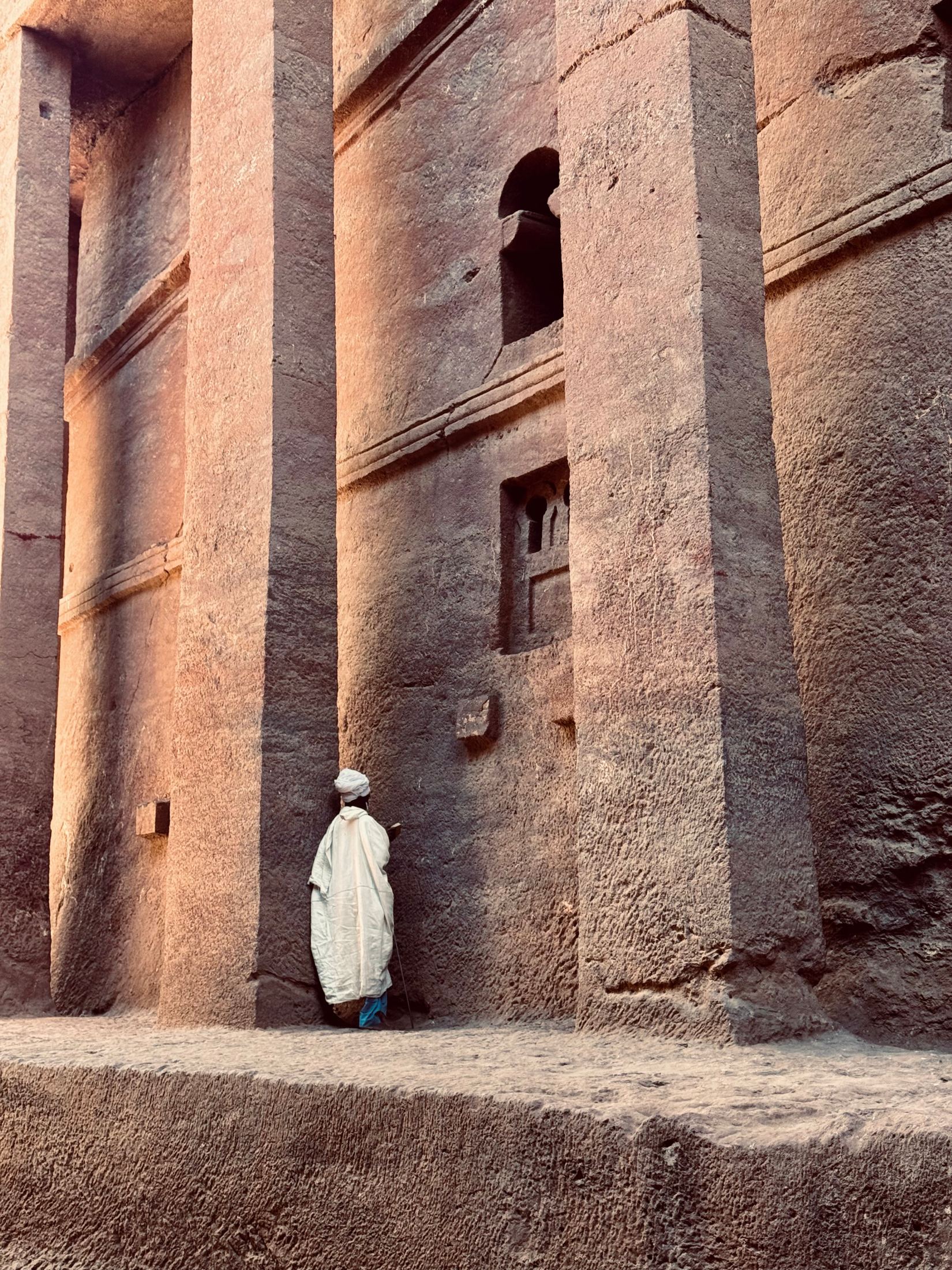 White-robed figure standing at the base of a towering rock-hewn church, Lalibela, Ethiopia