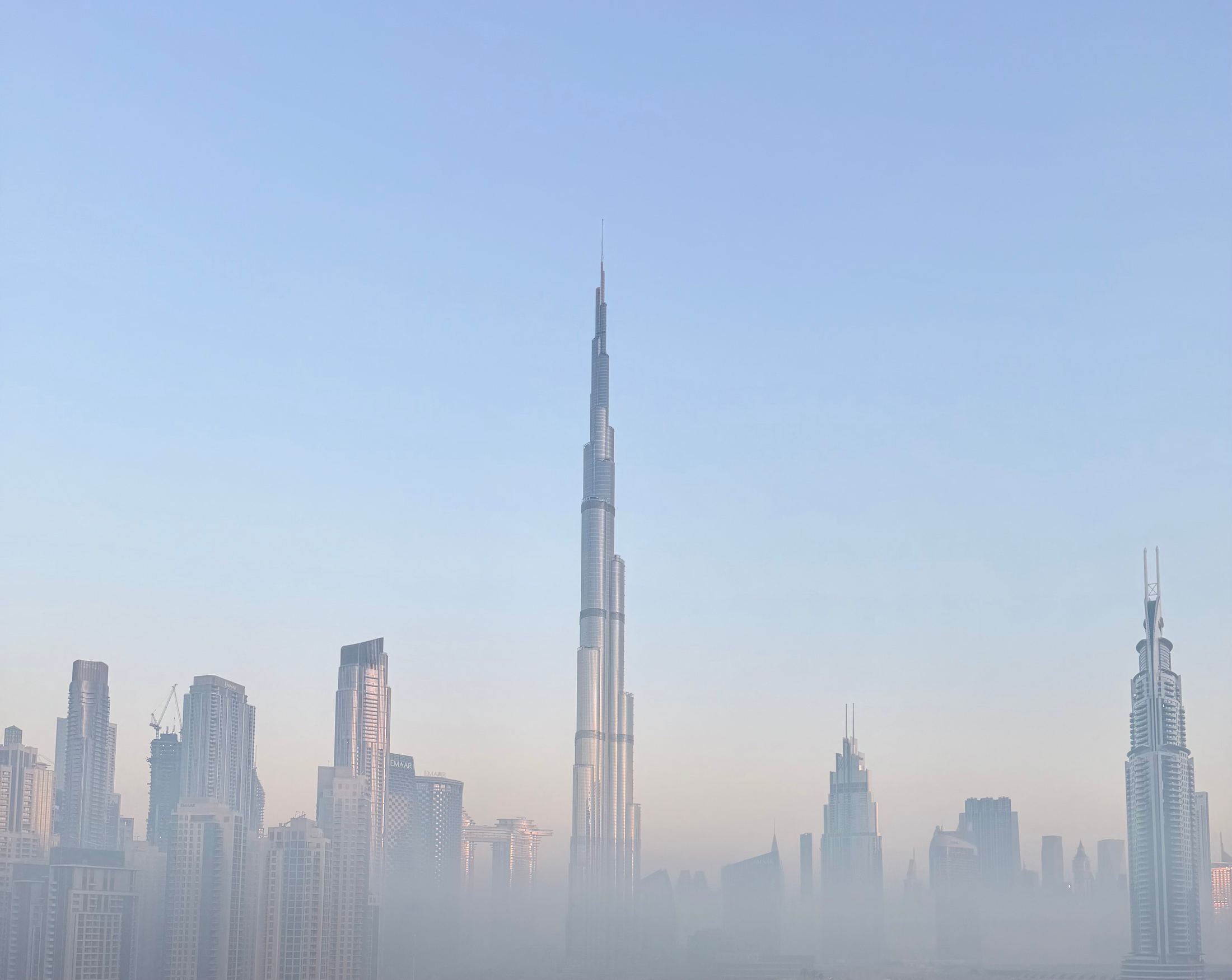 City skyline with a needle-thin supertall tower rising out of pale haze