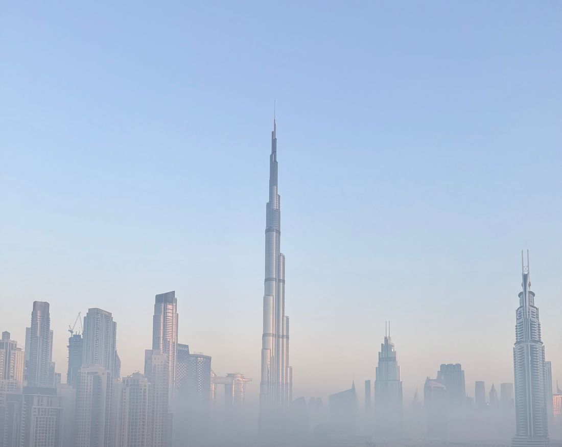 City skyline with a needle-thin supertall tower rising out of pale haze