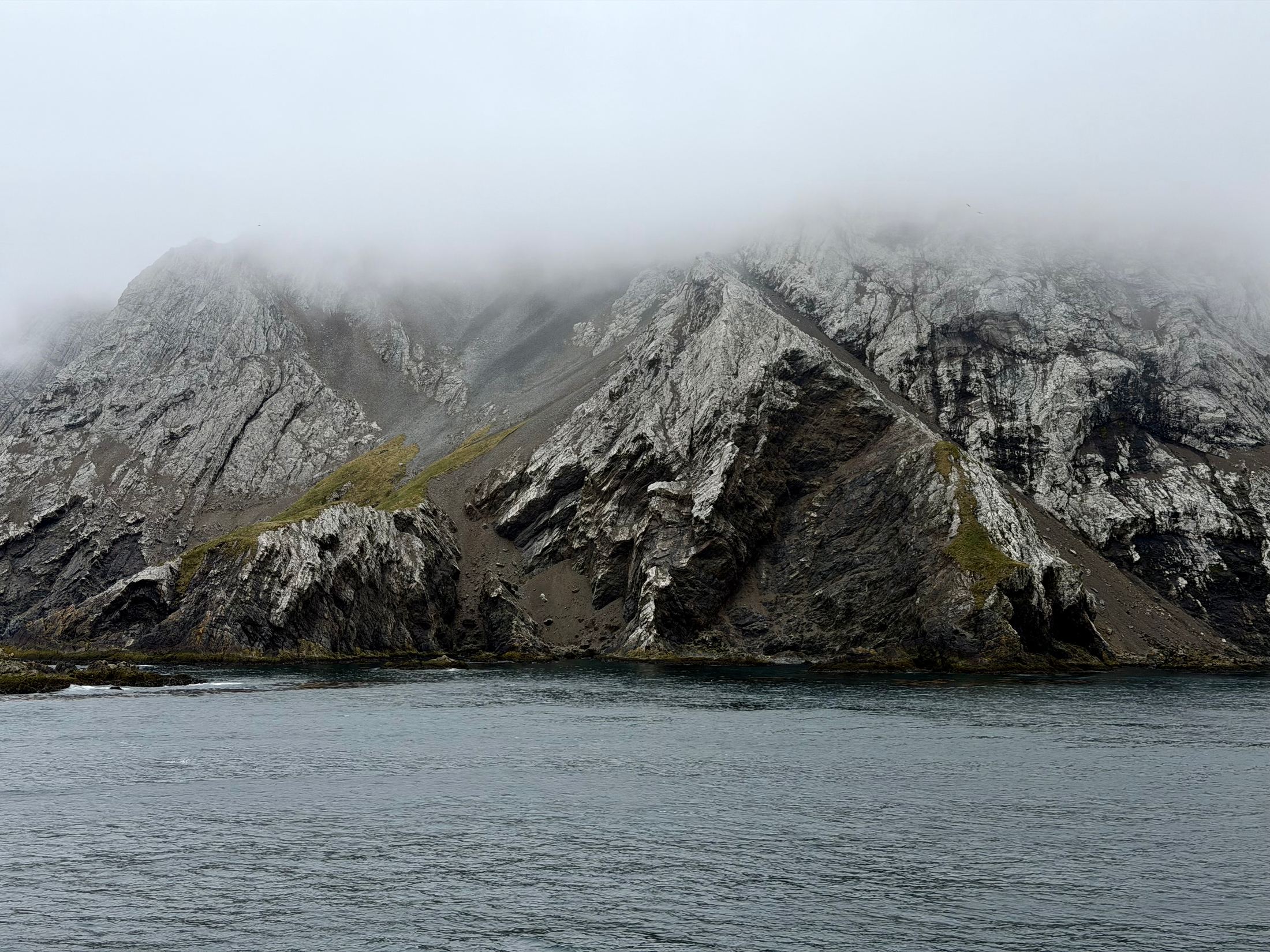 Steep rocky mountain capped in low cloud across calm grey water