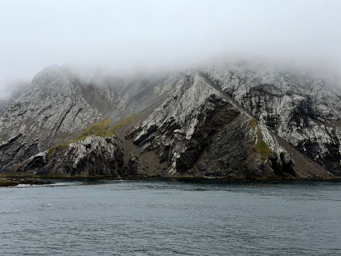 Steep rocky mountain capped in low cloud across calm grey water