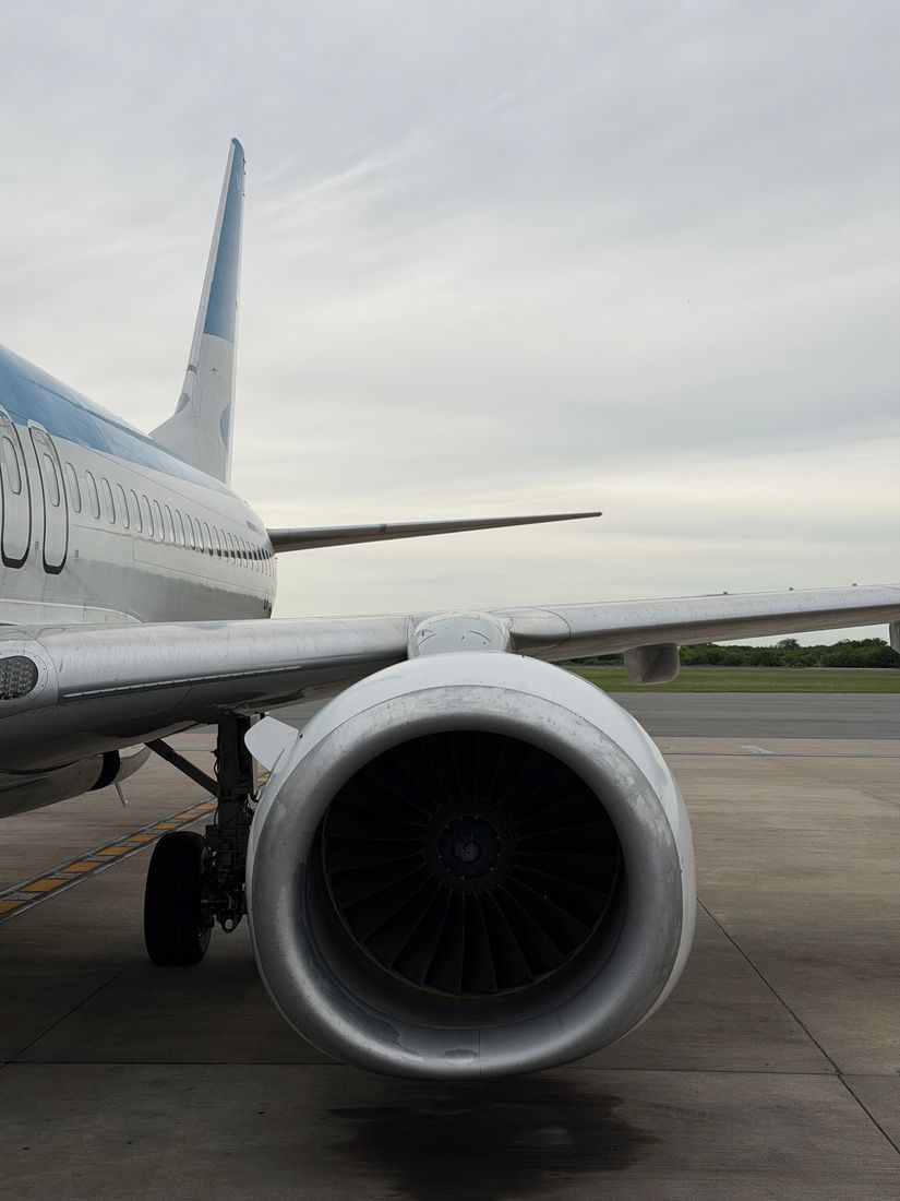 Jet engine and wing of an airliner parked on a grey apron