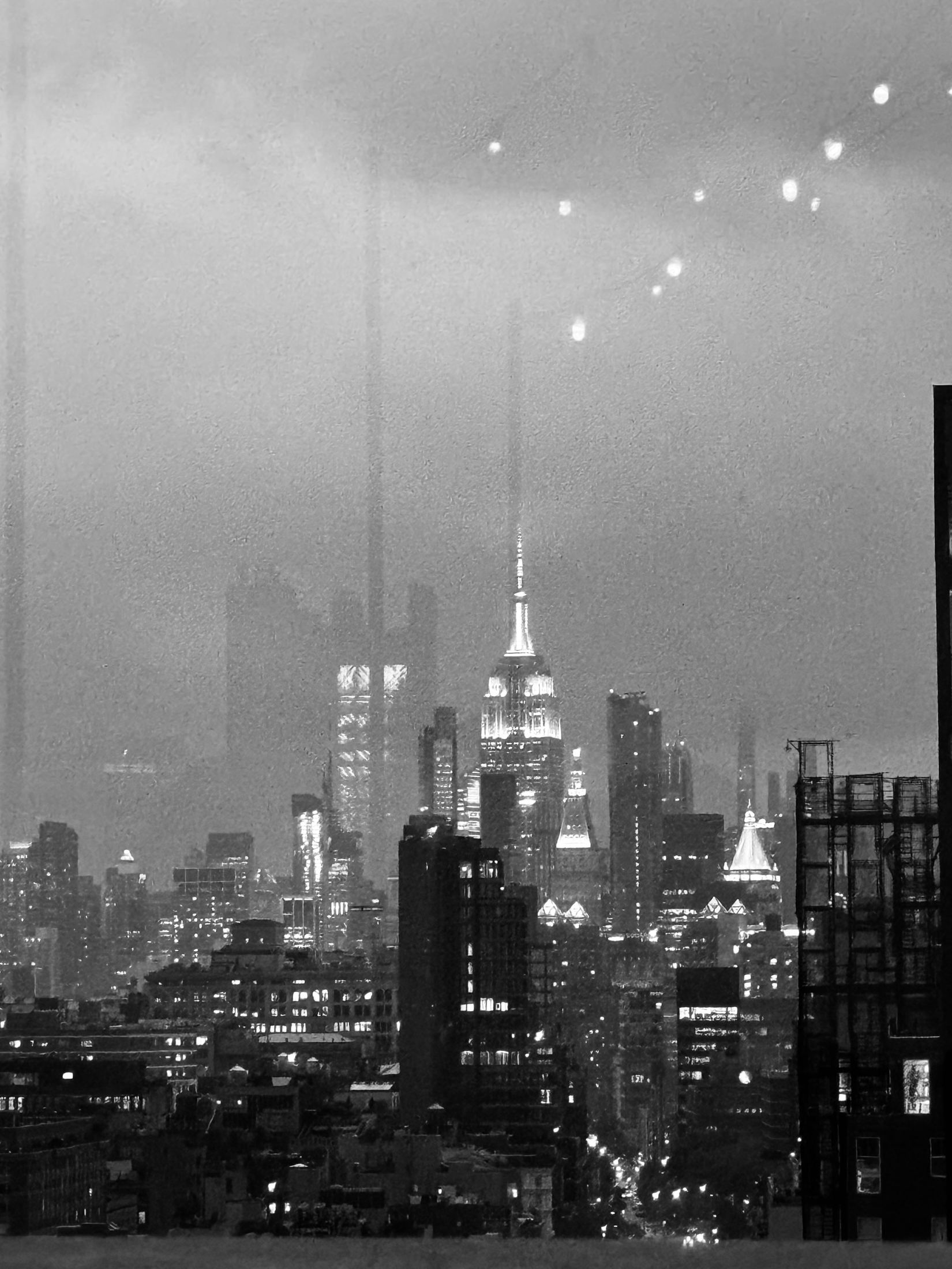 City skyline at night in black and white, a lit spire among the towers