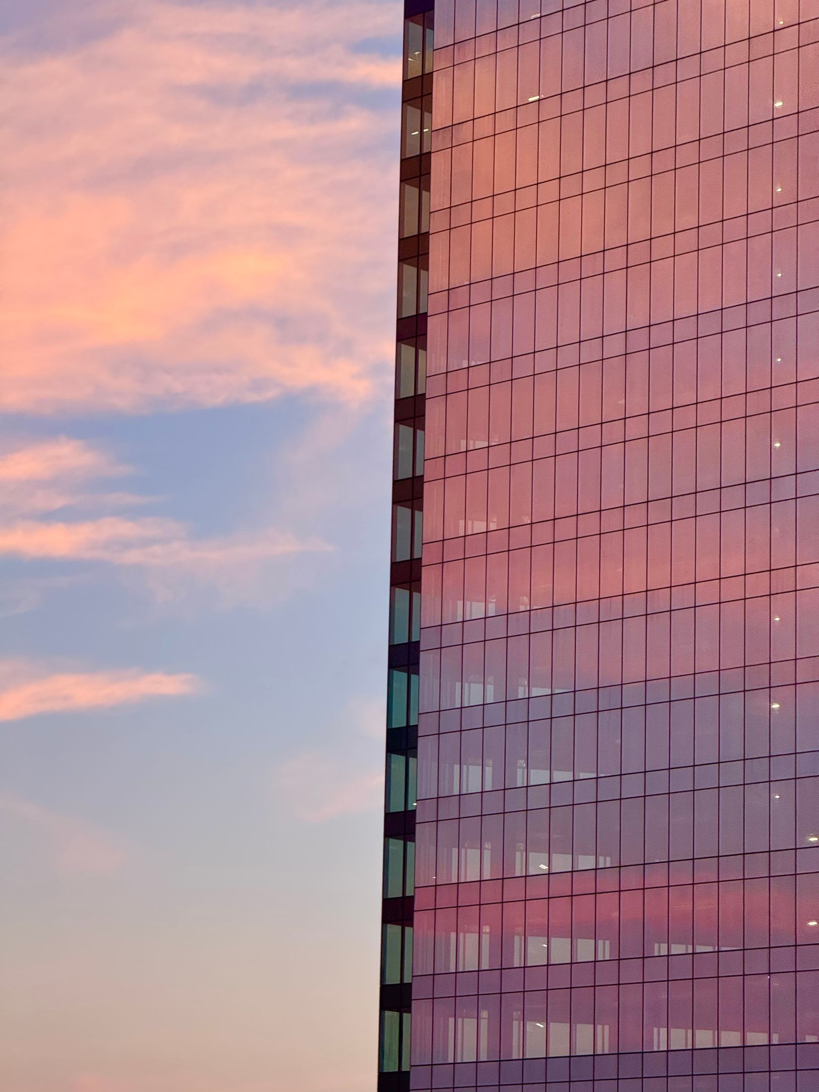 Glass tower reflecting a pink and gold sunset sky