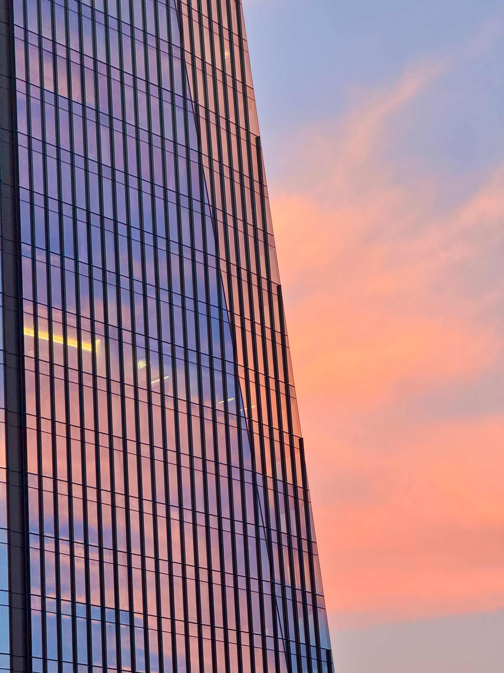 Tall glass facade rising into streaks of orange sunset cloud
