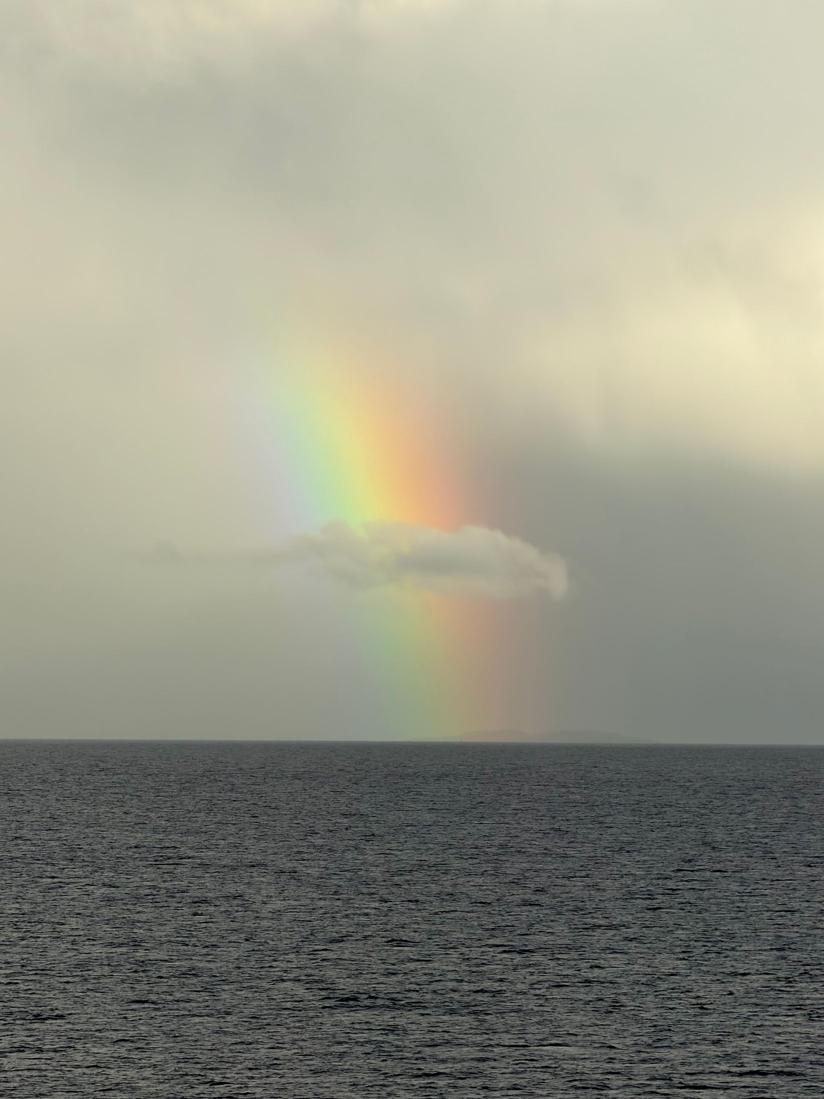 Rainbow dropping into a dark sea under heavy rain clouds